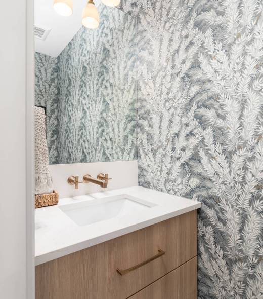 A bathroom with floral wallpaper, a floating wood vanity cabinet, marble countertop, and gold light fixture and faucet. A bathroom with floral wallpaper, a floating wood vanity cabinet, marble countertop, and gold light fixture and faucet.